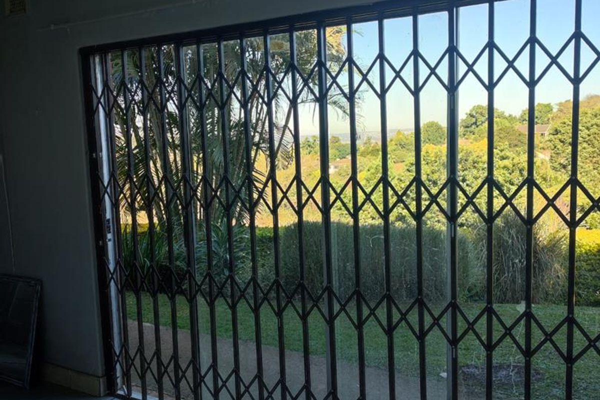 A bright, empty living area featuring large sliding glass doors with security gates, offering views of the garden and surrounding landscape.