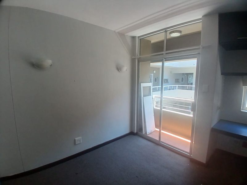 An empty bedroom featuring carpeted flooring, wall-mounted lighting, and a sliding glass door providing access to an exterior balcony area.