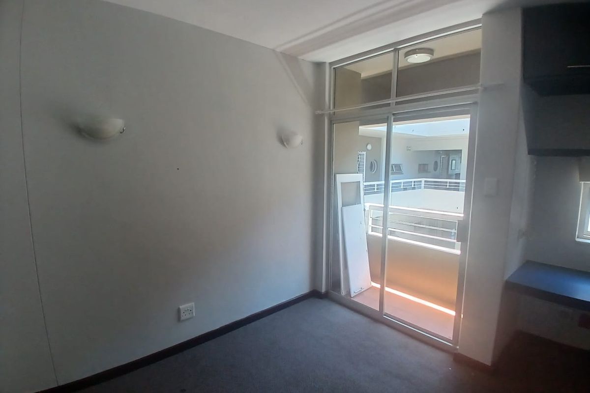 An empty bedroom featuring carpeted flooring, wall-mounted lighting, and a sliding glass door providing access to an exterior balcony area.