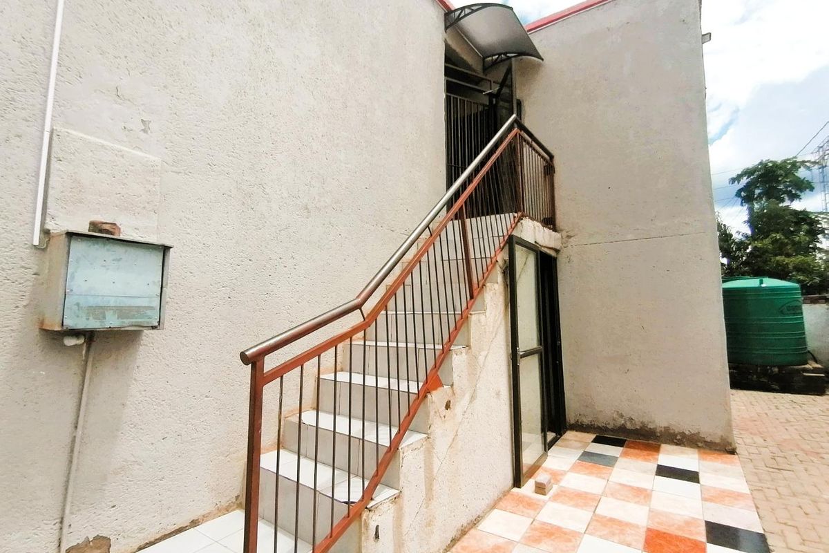 Exterior view of a rear staircase leading to an upper level, featuring tiled steps, metal railings, and a paved patio area.