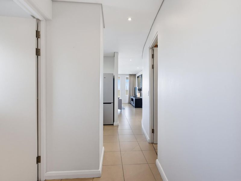 A clean, neutral hallway with tiled flooring and recessed lighting, providing access to the main living areas of the apartment.