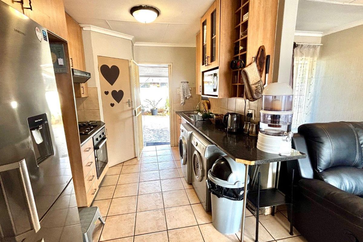 A functional kitchen and laundry area featuring wood-finish cabinetry, dark countertops, tiled flooring, and direct access to an outdoor patio space.