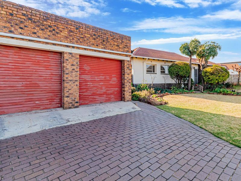 Front view of a residential property featuring a double garage with brick exterior, paved driveway, and a well-maintained front garden.