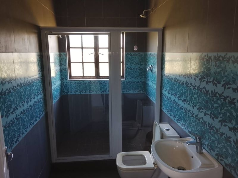 A functional bathroom featuring a shower enclosure, pedestal basin, and toilet, finished with decorative wall tiling and a window for natural light.