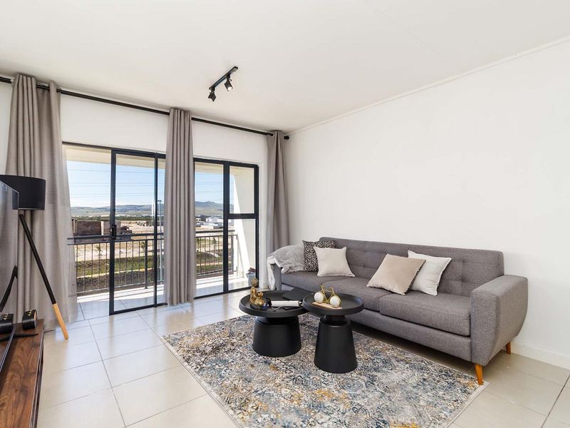 Bright living room featuring neutral tiled flooring and large sliding glass doors providing access to a balcony with scenic views.