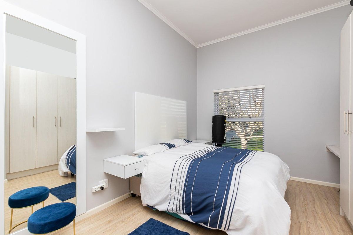 A well-maintained bedroom featuring light wood-look flooring, built-in cabinetry, a large mirror, and a window with fitted blinds.