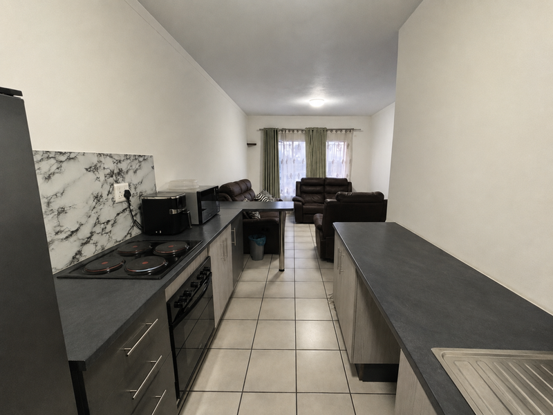Open-plan kitchen and living area featuring modern cabinetry, dark laminate countertops, electric hob, and neutral ceramic floor tiles throughout.