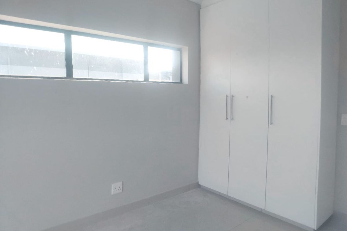 A clean, empty bedroom featuring neutral grey walls, tiled flooring, and white built-in cupboards with modern hardware.