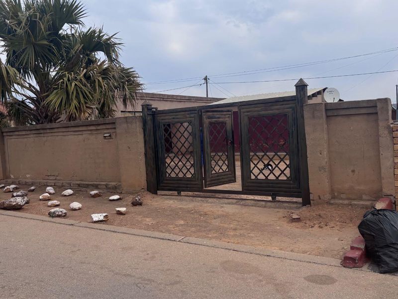 Front view of the property featuring a metal driveway gate and a perimeter wall boundary.