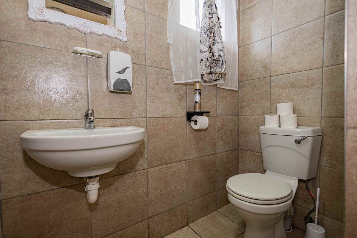 A compact bathroom featuring floor-to-ceiling ceramic wall tiles, a wall-mounted basin, and a standard white toilet suite.