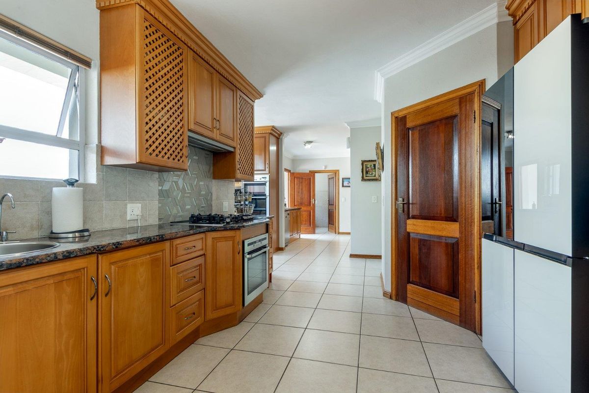 A functional kitchen featuring wooden cabinetry, granite countertops, a built-in oven and hob, and tiled flooring, leading into a hallway.