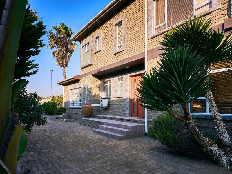 A well-maintained rear exterior view of a multi-story brick house featuring a paved patio area and established garden landscaping.