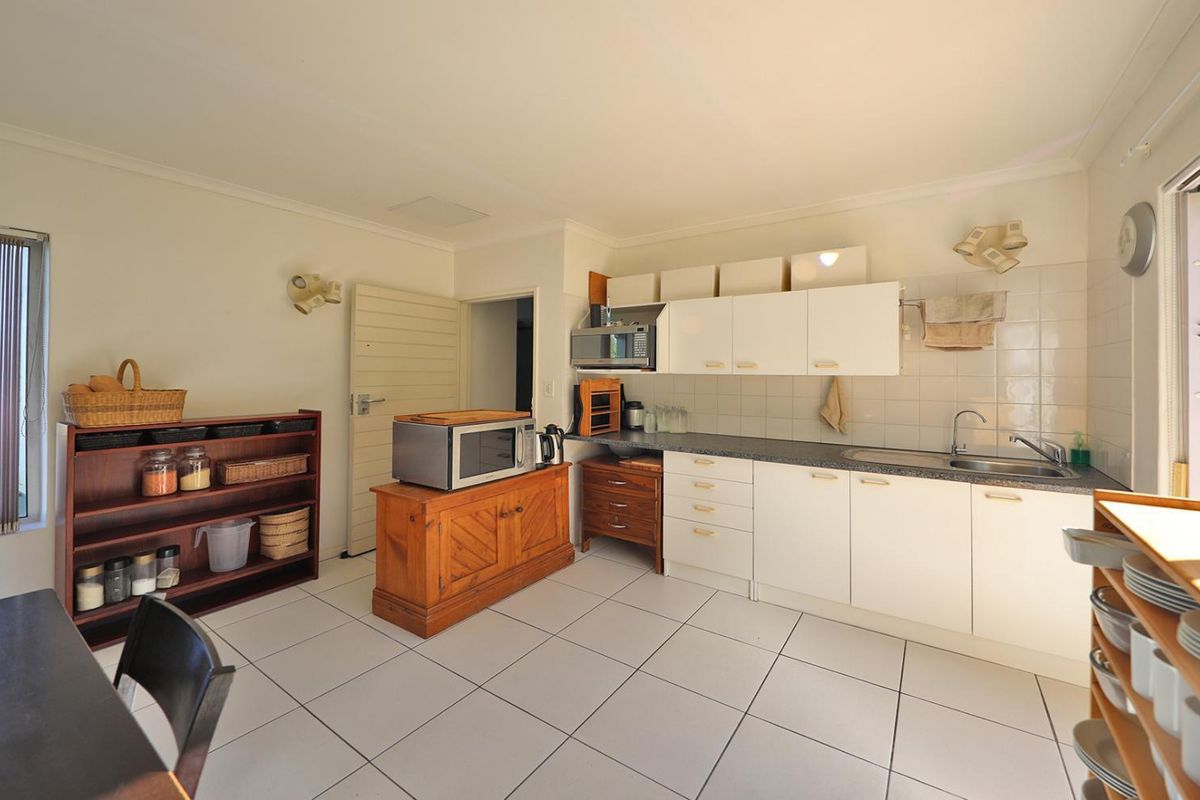 A functional kitchen featuring white cabinetry, tiled flooring, and a tiled splashback, with direct access to the outdoor area through sliding glass doors.
