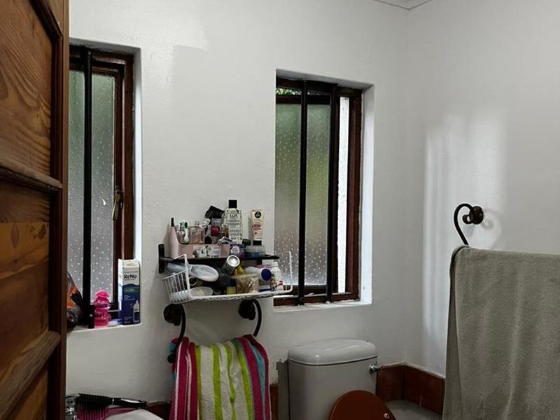 A functional bathroom featuring a pedestal basin, toilet, and dual windows with security bars, finished with simple white walls and coving.