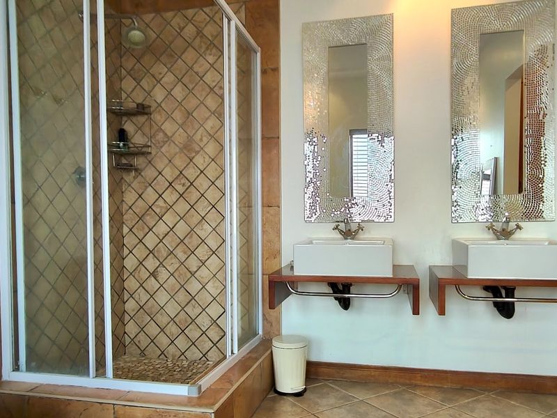 A bathroom featuring a glass-enclosed shower with tiled walls and a dual vanity setup with vessel sinks and decorative mirrors.
