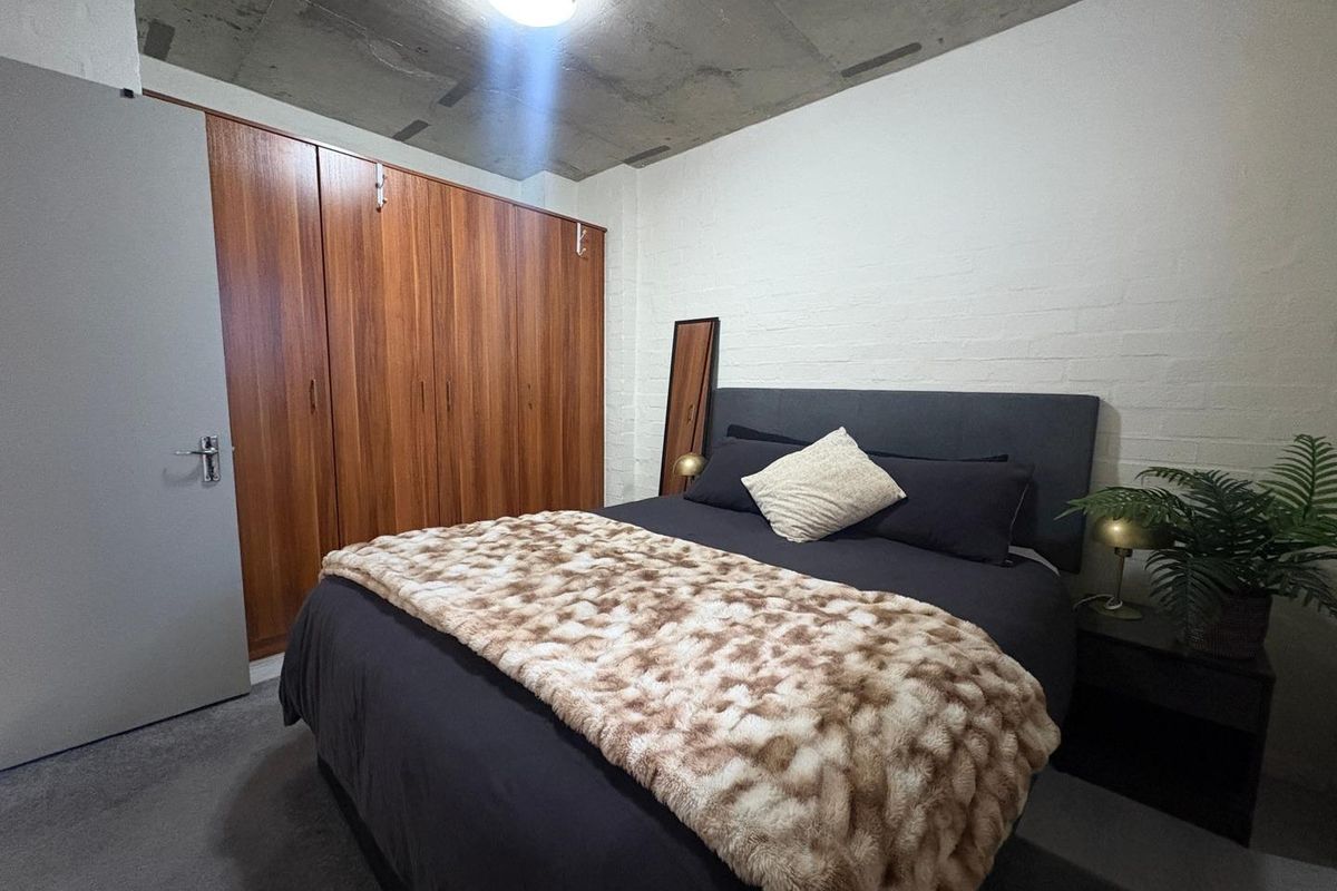 A bedroom featuring a raw concrete ceiling, built-in wooden wardrobes, and a painted brick wall finish.