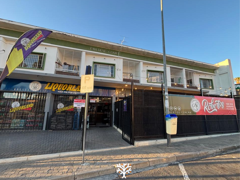 Front elevation of a mixed-use commercial building featuring ground-floor retail units, security fencing, and paved access area.