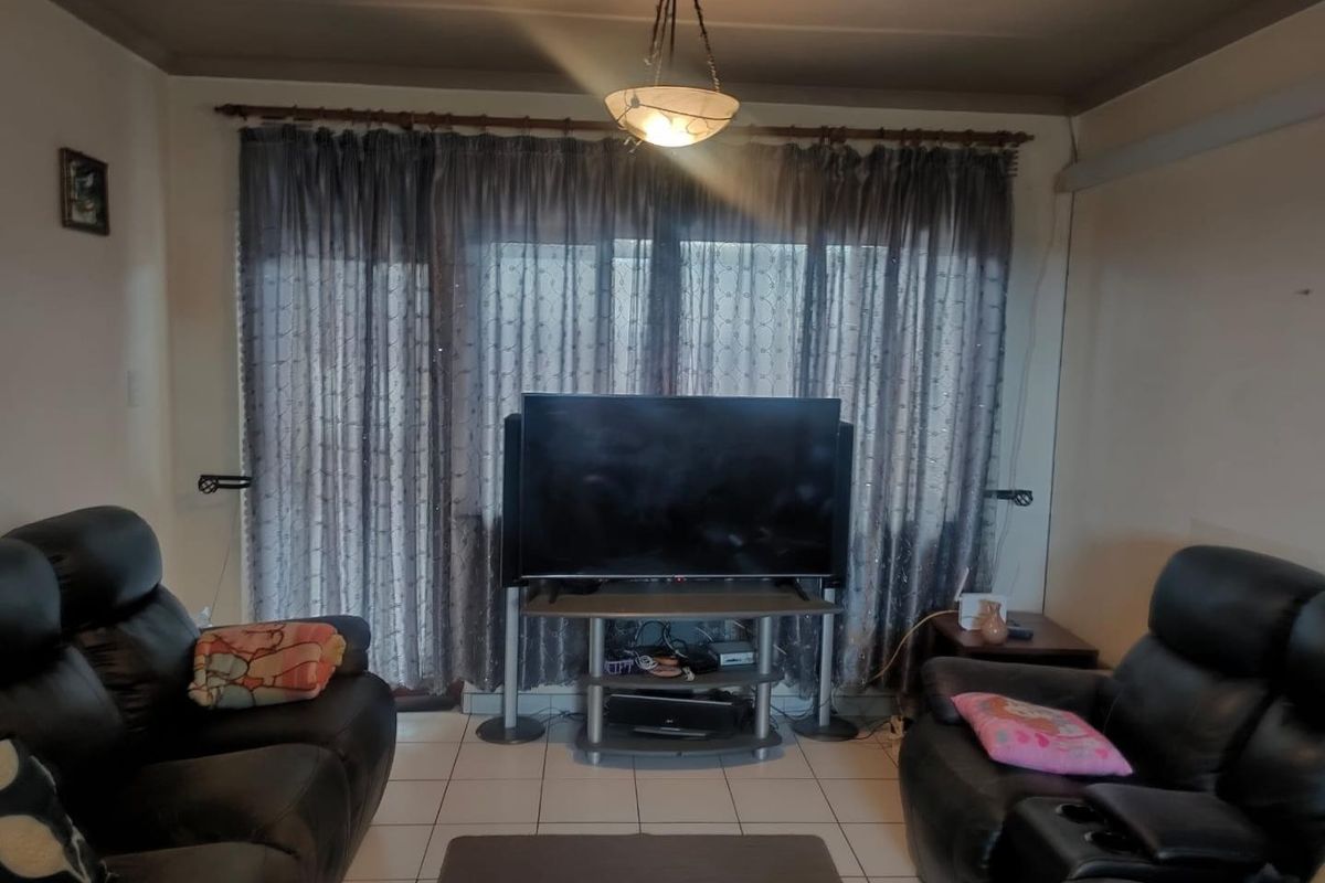 A living room featuring tiled flooring and a sliding glass door with curtains. The space requires cosmetic updates to the ceiling and wall finishes.