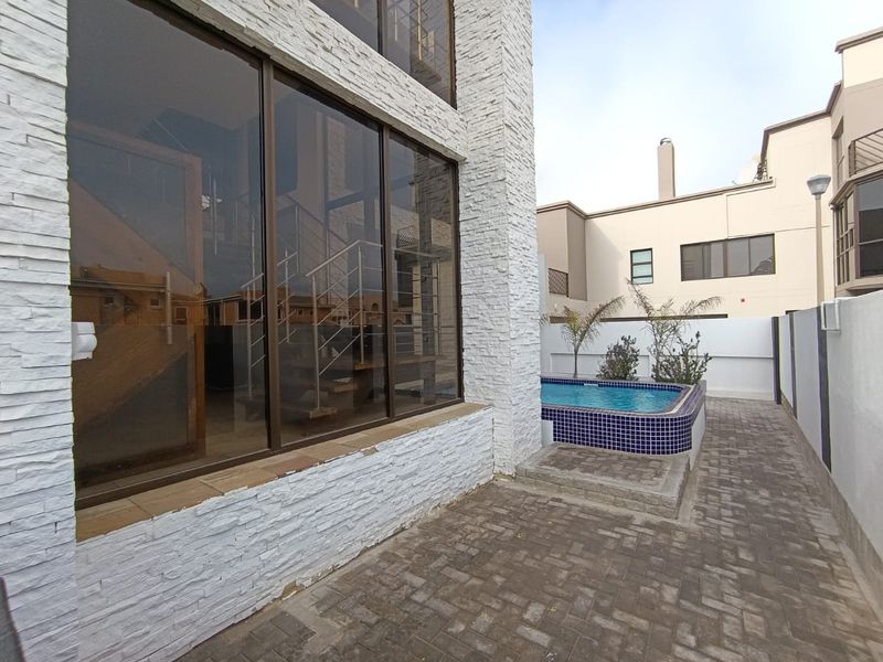 Exterior view featuring a small plunge pool, paved patio area, and modern stacked stone facade with large glass windows.