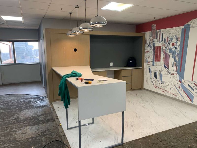Modern office space featuring built-in cabinetry, pendant lighting, and marble-look flooring, currently undergoing final floor finishing.