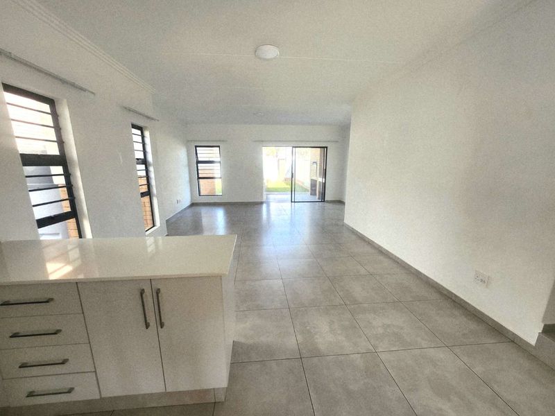 Spacious open-plan living area featuring neutral tiled flooring, modern kitchen cabinetry with quartz countertops, and large windows providing ample natural light.