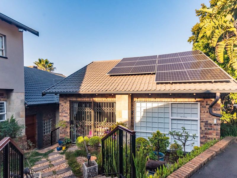 Rear view of the property featuring a brick facade, tiled roof with installed solar panels, and a landscaped garden area with paved walkway.