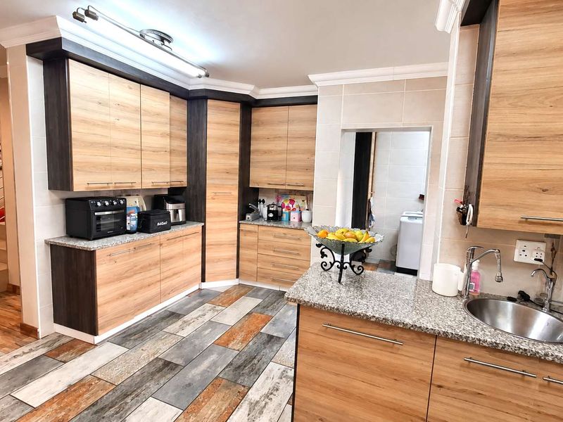 Modern kitchen featuring wood-grain cabinetry, granite countertops, stainless steel sink, and distinctive multi-toned tiled flooring, with an adjacent laundry area visible.