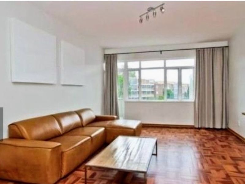 A bright living room featuring classic parquet flooring, large windows with curtains, and a modern ceiling spotlight fixture.
