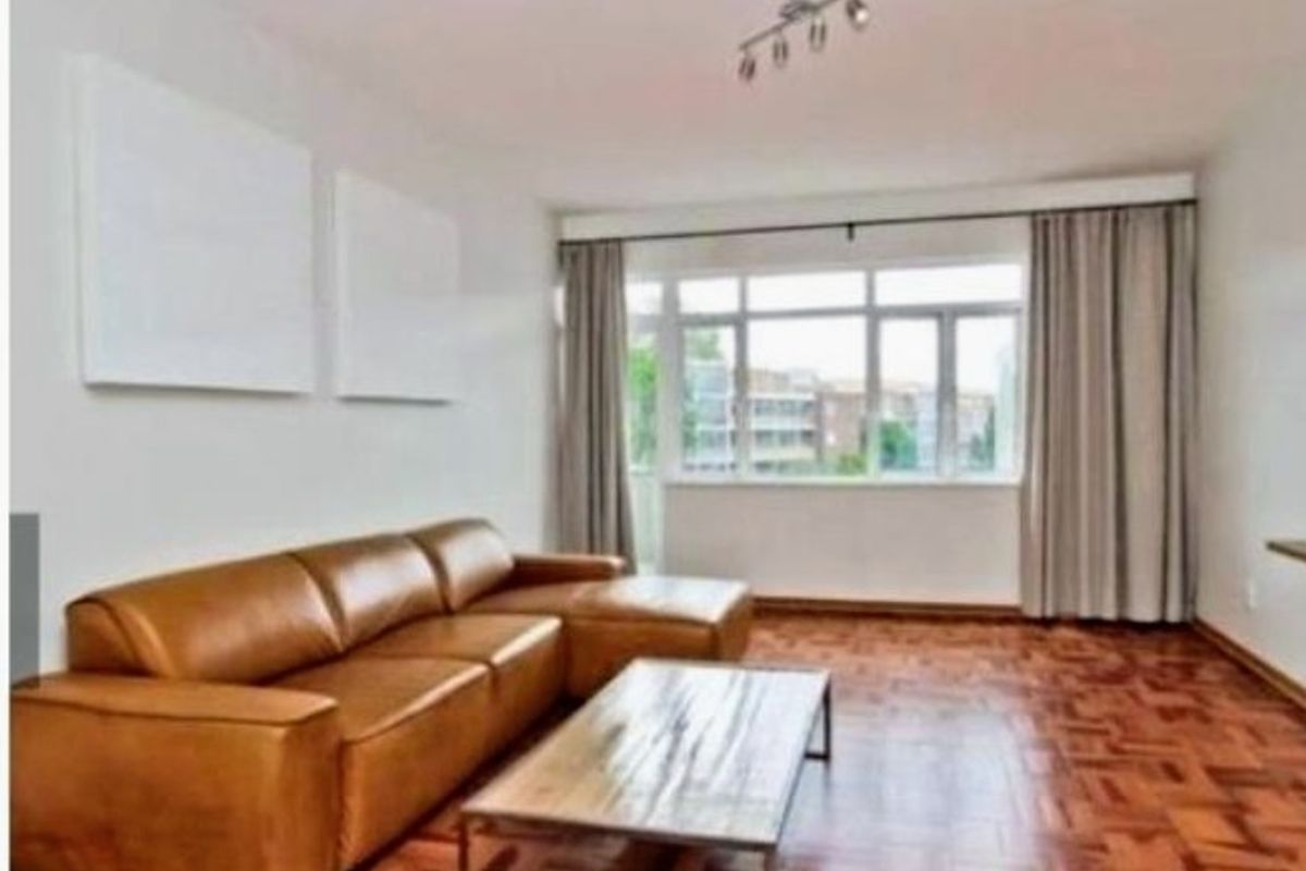 A bright living room featuring classic parquet flooring, large windows with curtains, and a modern ceiling spotlight fixture.