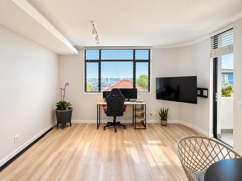 Bright living area featuring light wood-look laminate flooring, track lighting, and a sliding glass door leading to an outdoor space.