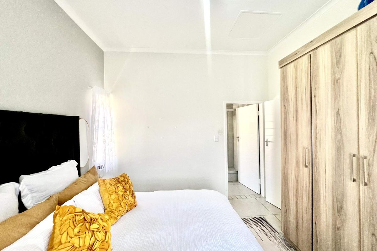 A bedroom featuring built-in wooden cabinetry and an en-suite bathroom entrance, finished with tiled flooring and neutral wall tones.