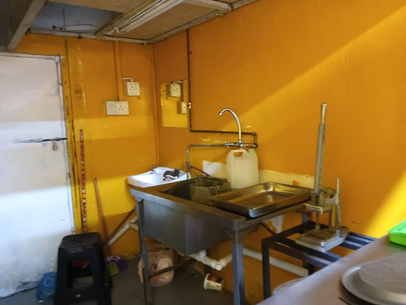 A functional scullery or prep area featuring a stainless steel sink, exposed plumbing, and basic utility finishes.