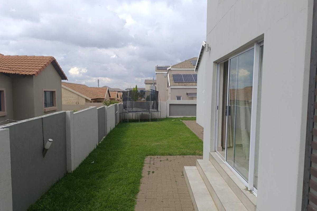 A side garden area featuring a paved walkway, lawn, and sliding glass door access to the main dwelling.
