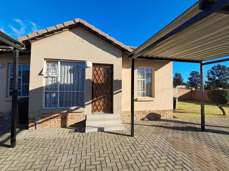 Front elevation of a townhouse featuring a paved driveway, covered carport, and secure entrance with a security gate.