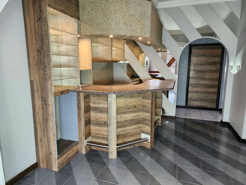A well-maintained built-in bar area featuring wood-look cabinetry, stone countertops, recessed lighting, and decorative tiled flooring, situated within an arched architectural space.
