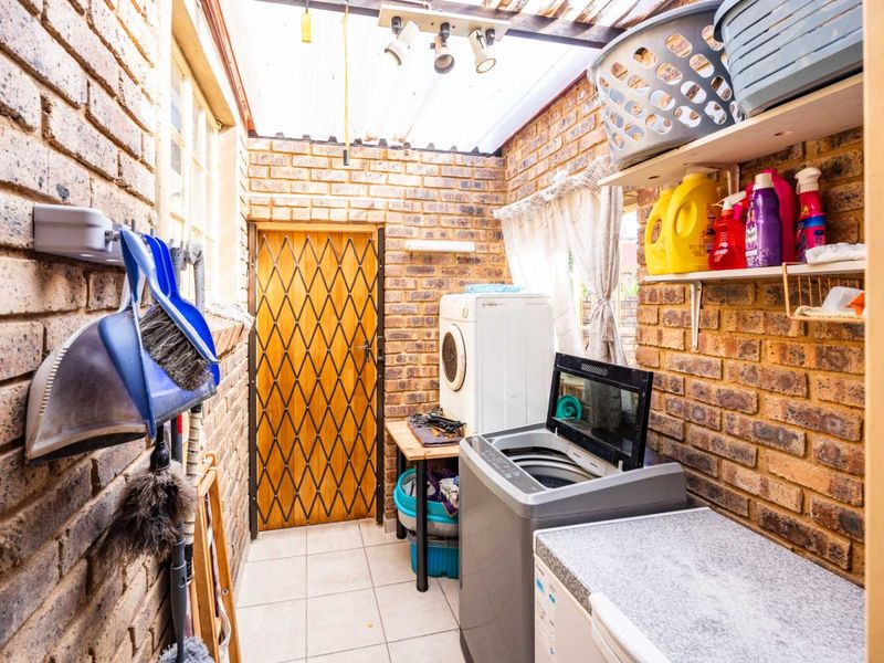 A functional laundry area featuring exposed brick walls, tiled flooring, and a translucent roof, providing a practical space for washing and utility tasks.