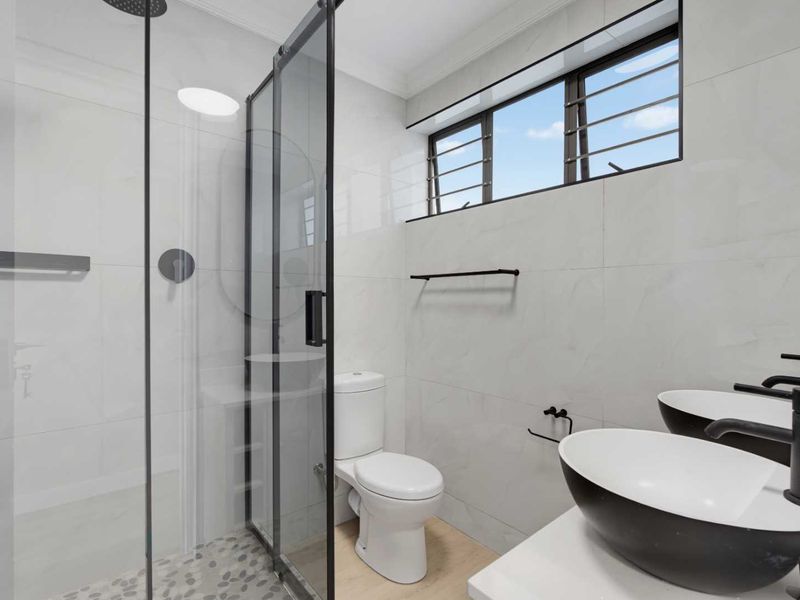 Modern bathroom featuring a glass-enclosed shower, dual vessel sinks with matte black fixtures, and clean tiled finishes.