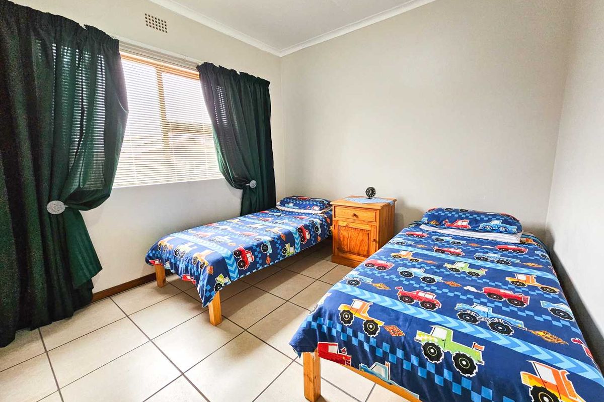 A functional bedroom featuring tiled flooring, a window with blinds, and neutral wall finishes.