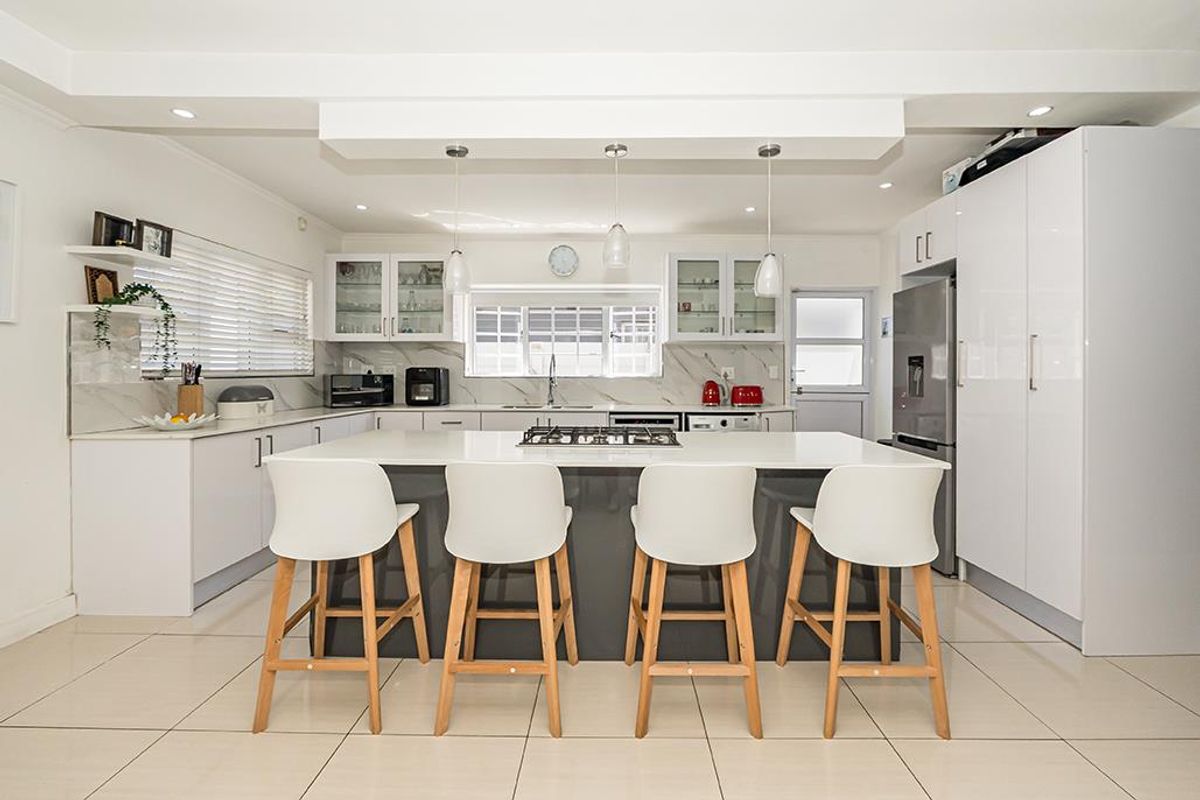 Modern kitchen featuring a central island with a built-in gas hob, white cabinetry, marble-look splashbacks, and tiled flooring.