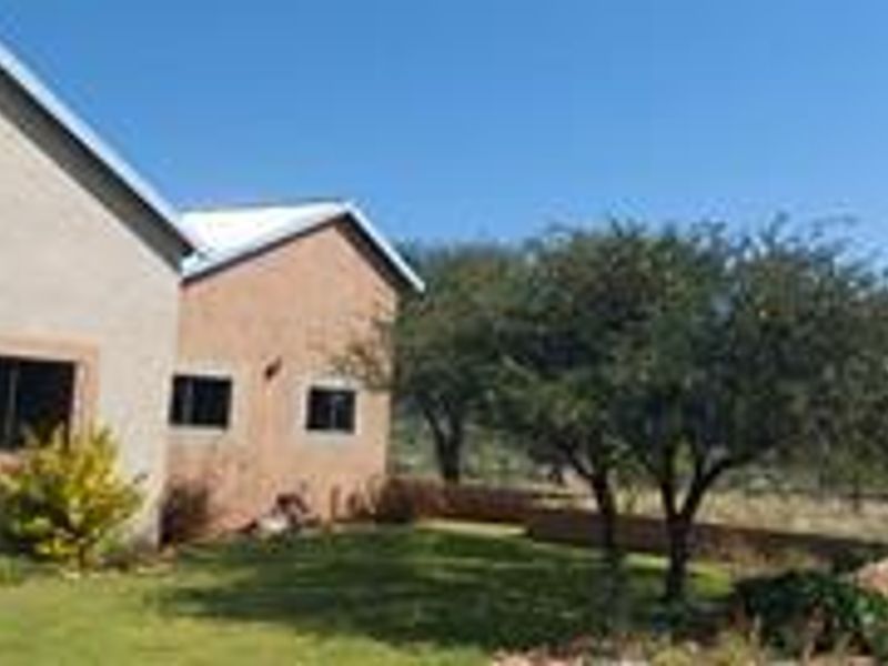 Rear view of the property featuring a stucco facade, metal roofing, and a landscaped garden area with a low retaining wall.