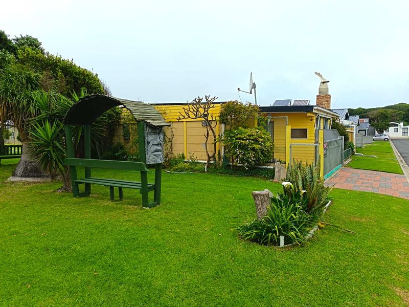 Front view of a yellow timber-clad house featuring a brick chimney, solar panels, and a well-maintained lawn with established garden elements.