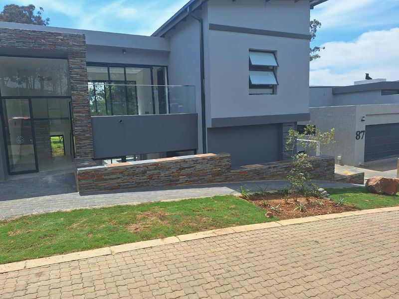 Modern cluster home exterior featuring contemporary stone cladding, glass balustrades, and a neat paved driveway with landscaped garden elements.