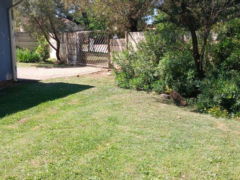 A view of the rear garden area featuring a lawn, paved driveway, and perimeter boundary wall with a metal security gate.