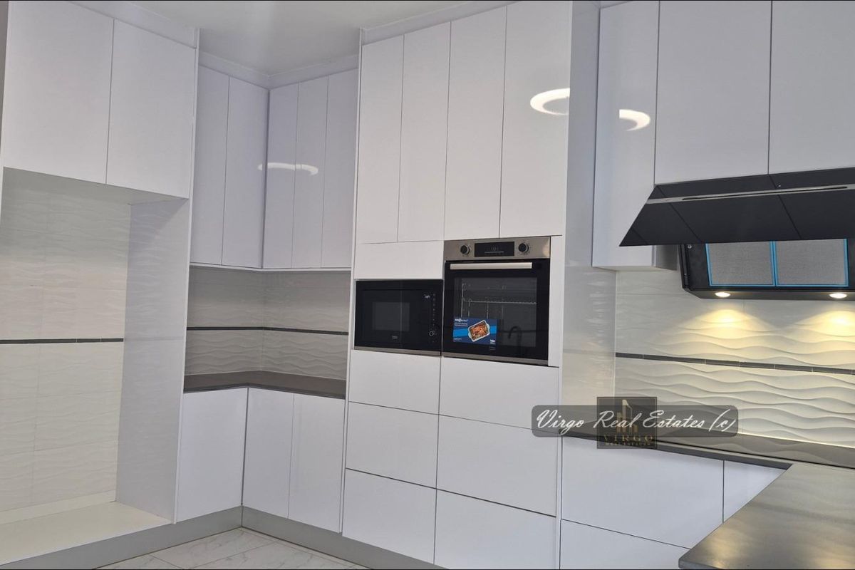 Modern kitchen featuring high-gloss white cabinetry, integrated appliances including an oven and microwave, and a stylish textured tile backsplash.