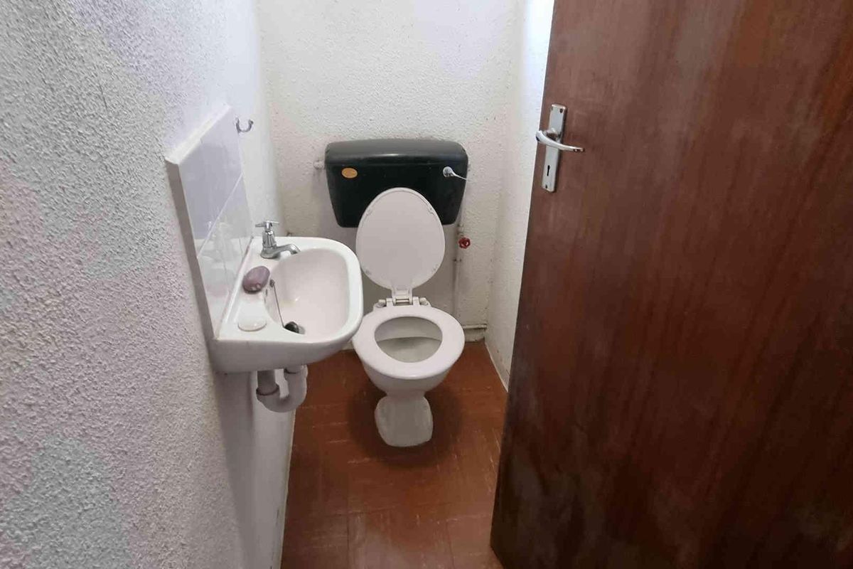 A compact bathroom featuring a wall-mounted basin and a standard toilet with dated finishes and flooring.