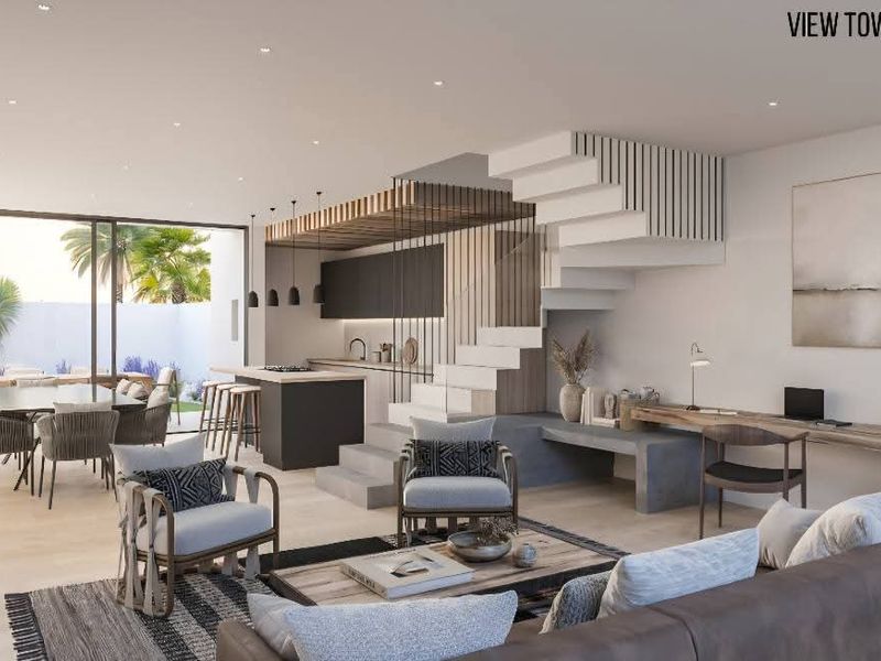 Modern open-plan living area featuring a sleek kitchen, integrated staircase, and seamless flow to the outdoor patio and garden through large sliding doors.
