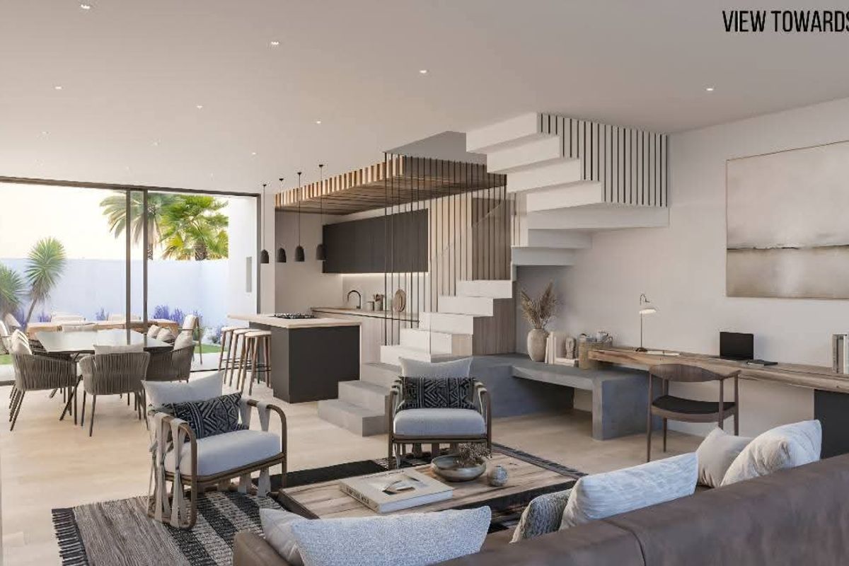 Modern open-plan living area featuring a sleek kitchen, integrated staircase, and seamless flow to the outdoor patio and garden through large sliding doors.