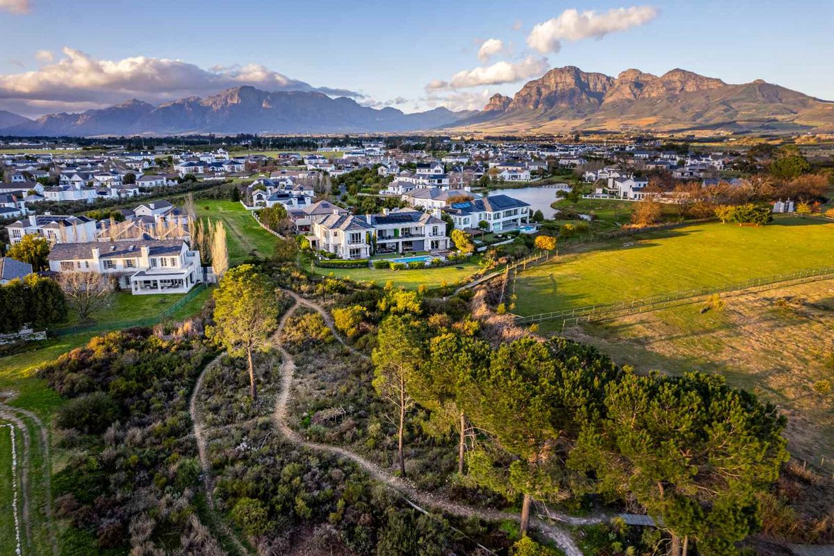 An elevated aerial view of a residential estate featuring well-maintained homes, expansive green spaces, and a scenic mountain range in the background.