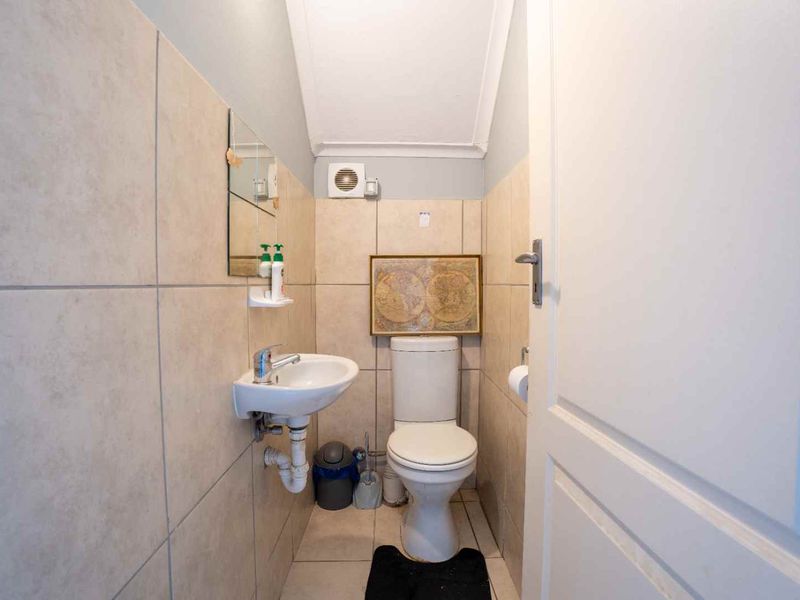 Compact guest bathroom featuring a wall-mounted basin, toilet, and extractor fan with neutral wall and floor tiling.