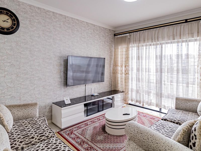 A well-maintained living room featuring textured wallpaper, cove molding, and a large sliding glass door providing access to the balcony.